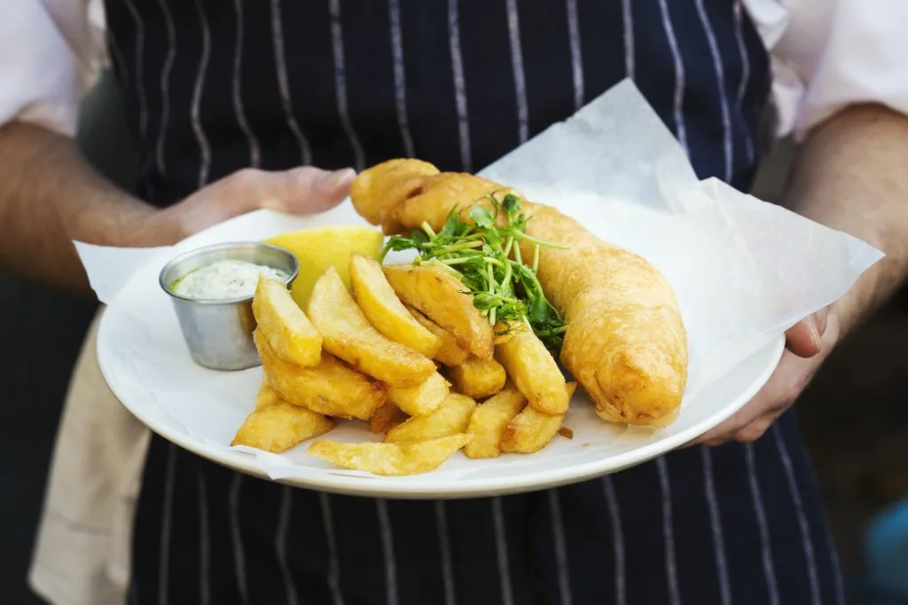A cooked meal, a dish of fish and chips with garnish and tartare sauce.