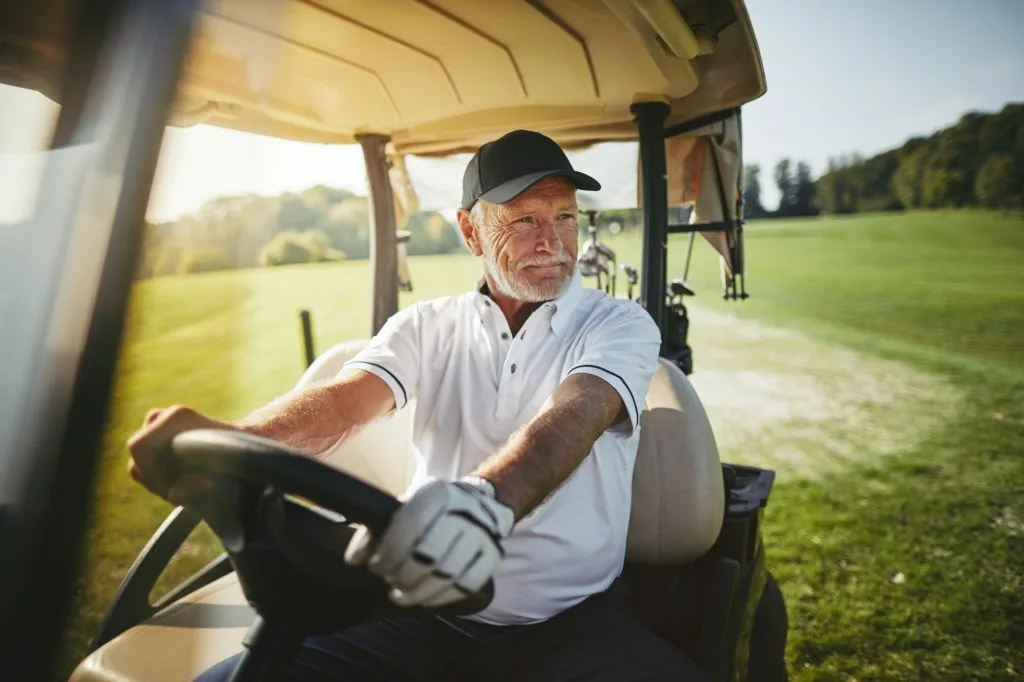 Senior man driving his golf cart on a fairway